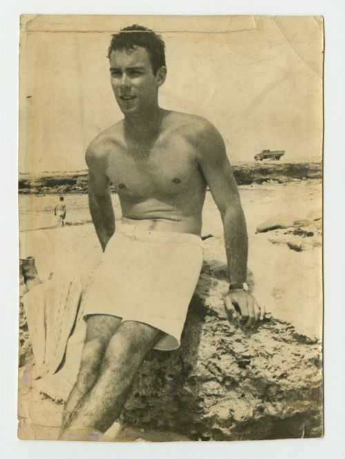 Arthur Howe, Jr. on a beach in North Africa, sitting on a rock. Photograph verso.